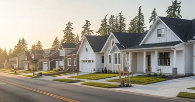 A row of brand new single-family homes on a quiet suburban street in the Portland metro under soft golden morning light