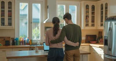A couple standing at a kitchen island in a bright new home looking at a laptop together