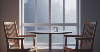Two empty chairs facing each other across a small table by a window, set up for a conversation