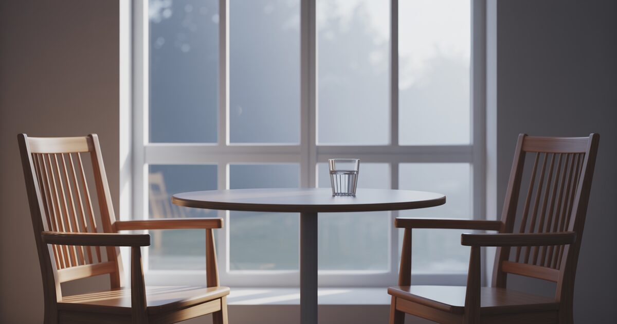 Two empty chairs facing each other across a small table by a window, set up for a conversation